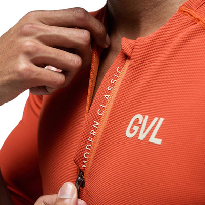 Close-up of the chest area of a Givelo Modern Classic half-zip jersey in a vibrant pumpkin color. The image shows the texture of the waffle fabric, the neatly crafted zipper, and the bold 'GVL' branding on the right side.