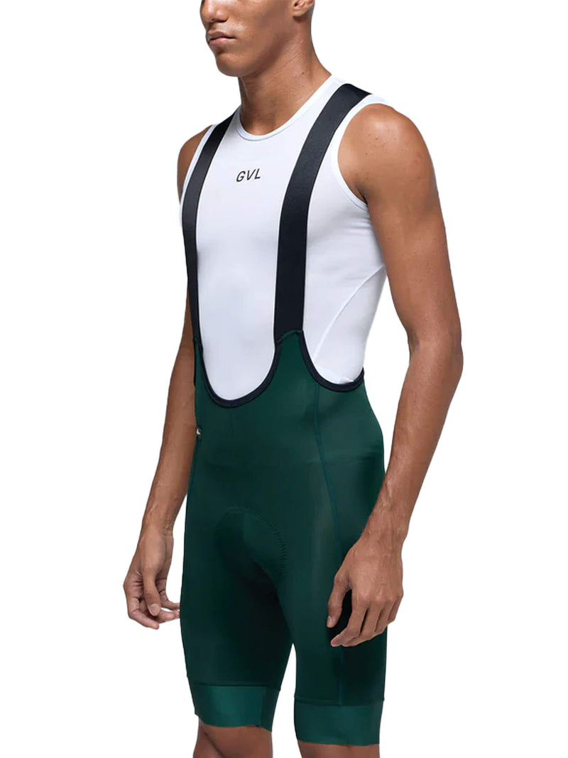 A side view of a man wearing Givelo Classic Bib Shorts. The bib shorts have a sleek design with a white upper body, black shoulder straps, and dark green lower half. The GVL logo is subtly placed on the chest area. The garment appears to be made from a high-performance fabric that looks moisture-wicking and form-fitting, suitable for cycling activities.