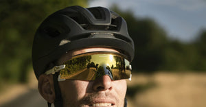 Male cyclist wearing oakley aro5 race helmet in matte black wearing Oakley Encoder glasses with gold lenses and white frame