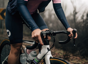 person riding a road bike wearing the black sheep essential bib in black, black arm warmers and pink essential TEAM jersey