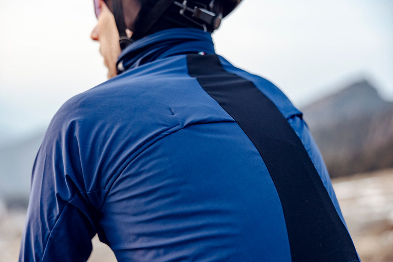 Rear perspective of a cyclist wearing the Q36.5 Bat Jacket in navy, showcasing the strategic ventilation openings for moisture control.