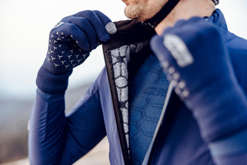 Close-up of a cyclist adjusting the hermetic collar on the Q36.5 Bat Jacket in navy, indicating the weatherproof and comfort features.