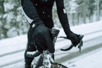 Cyclist in winter gear riding in the snow, wearing black thermal gloves from Q36.5.