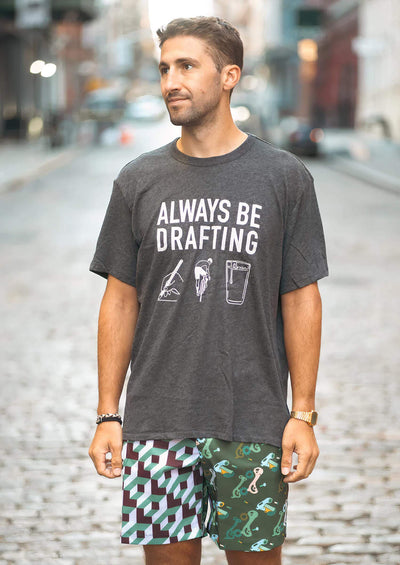 Man wearing Ostroy Grey "Always Be Drafting" tee shirt with cycling and beverage graphics.