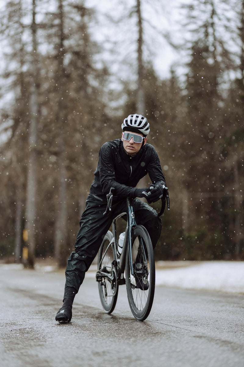 Cyclist wearing Q36.5 Rain Overpants in wet conditions, demonstrating visibility and protection.