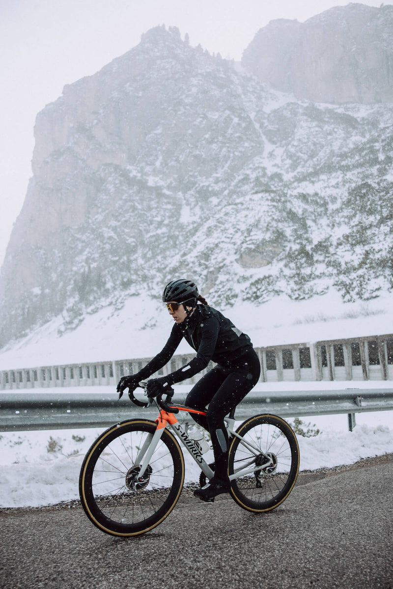 A cyclist in motion wearing Q36.5 Winter Bib Tights, illustrating the ergonomic fit and comfort during a snowy mountain ride.