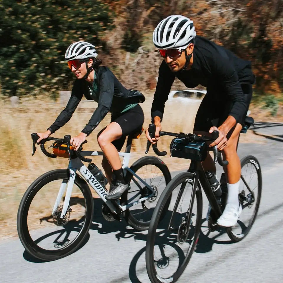male and female cyclist riding bikes equipped with ALMSTHRE compact signature bag in gold and signature bag in black.