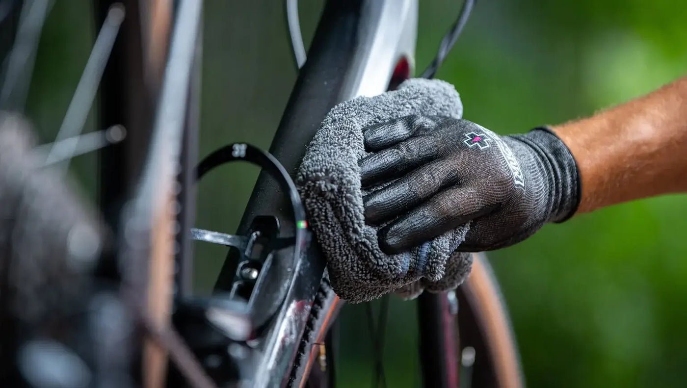 cyclist with Muc-off rubber gloves using Muc-off bike cleaning solution with non-abrasive cloth to clean his bike