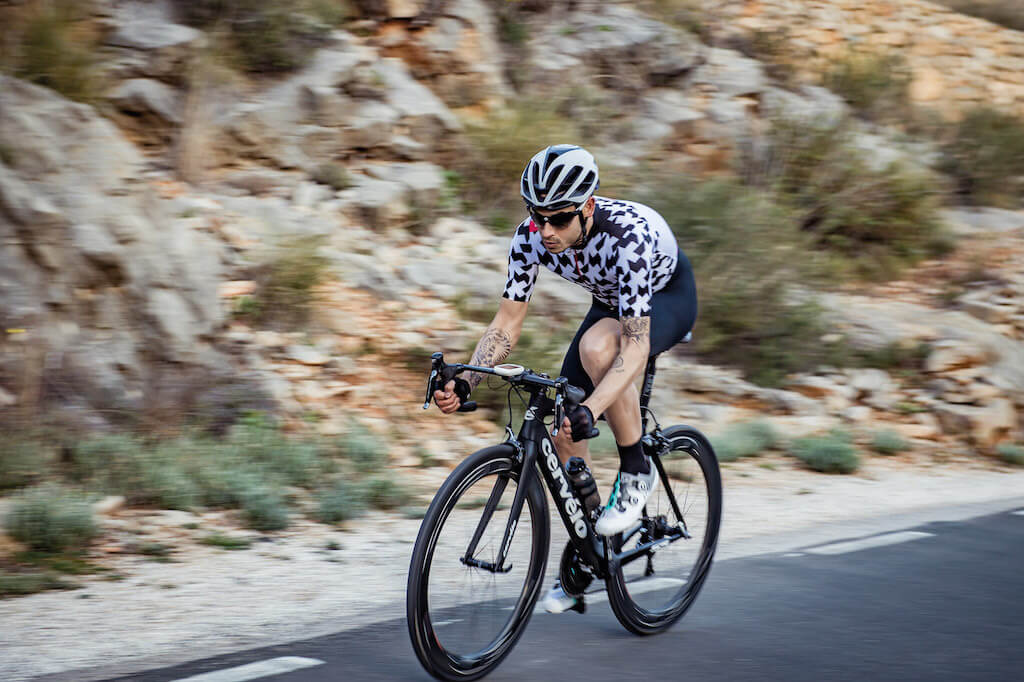 male cyclist riding a cervelo wearing an assos jersey and assos bibs with assos gloves
