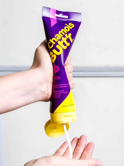 An image of an 8oz bottle of Unisex Chamois cream by Chamois Butt'r being squeezed onto a cyclists hand, this is a premium chamois cream for any cyclist.