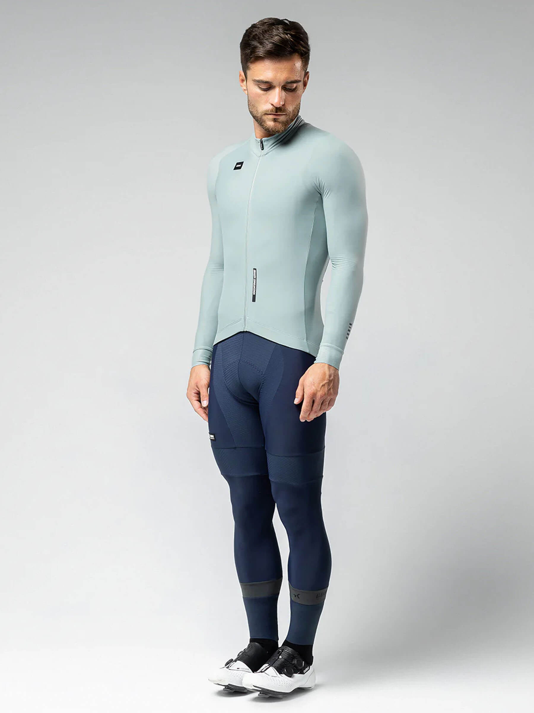Man wearing GOBIK Pacer Solid Long Sleeve Jersey - Men's in light blue with navy cycling pants on gray background