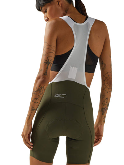 Rear view of a woman in olive green Givelo HD Pro Bib Shorts paired with a white mesh cycling vest. The shorts feature high compression and fabric designed for long cycling sessions, with a focus on the ergonomic fit and padding.