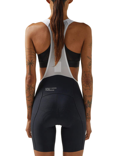 Rear view of a woman wearing black Givelo HD Pro Bib Shorts with white shoulder straps, emphasizing the shorts' ergonomic fit and the mesh vest's breathability, suited for professional and long-distance cycling.