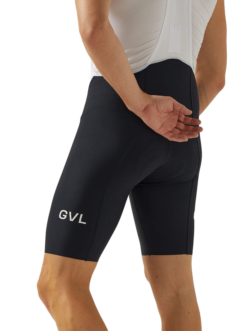 Side view of a man wearing black Givelo HD Pro Bib Shorts, with the "GVL" logo on the thigh. These shorts are designed with a snug fit and have a smooth texture to facilitate comfort and performance on long rides.