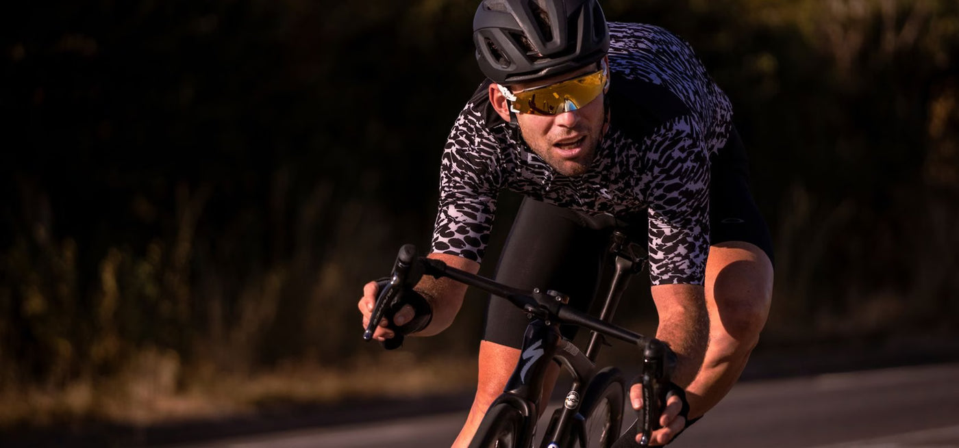 Mark Cavendish cyclist riding bike while wearing oakley black Aro5 race helmet and limited Cavendish Encoder oakly glasses in gold and white