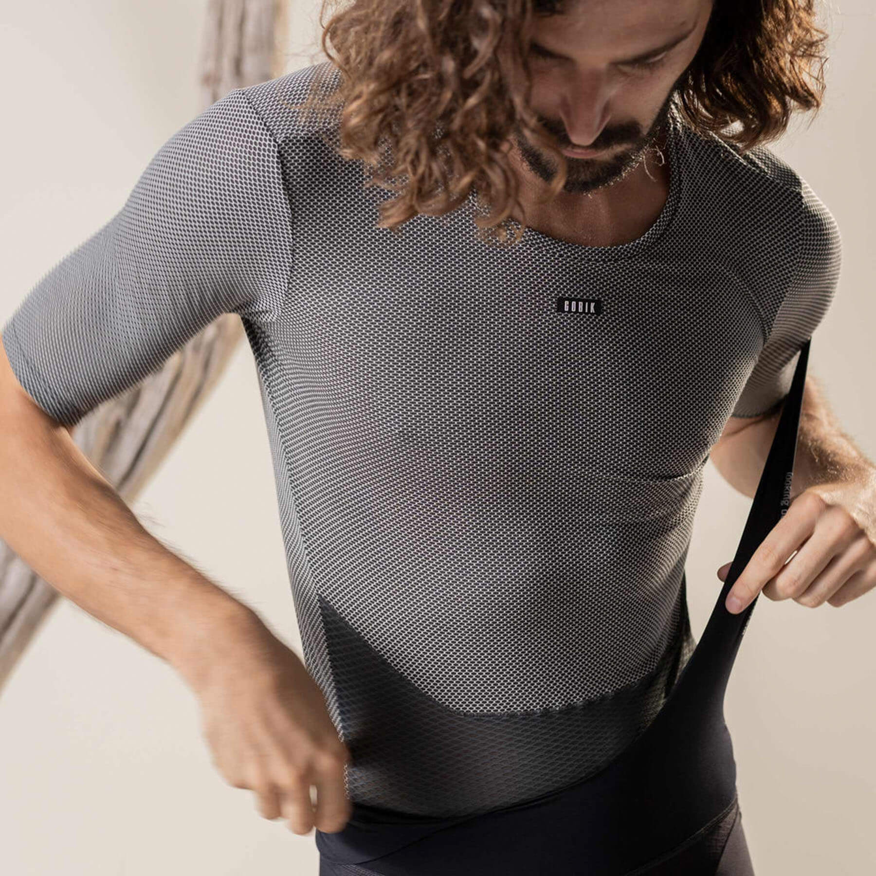 A front view of a man's torso, wearing a grey, short-sleeved base layer cycling shirt with a hexagonal mesh structure. The lower part of the shirt has a dense mesh pattern.