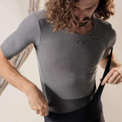 A front view of a man's torso, wearing a grey, short-sleeved base layer cycling shirt with a hexagonal mesh structure. The lower part of the shirt has a dense mesh pattern.