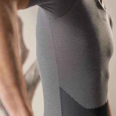 A close-up of a man's torso from the side, wearing a black, short-sleeved base layer cycling shirt. The fabric has a hexagonal mesh structure for breathability, with a solid black lower panel.