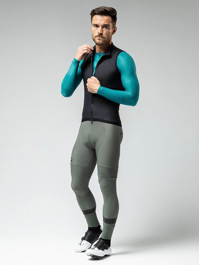 Male cyclist wearing Gobik Men's Crow Vest, black with teal sleeves, for aerodynamic performance in 10-18ºC weather.