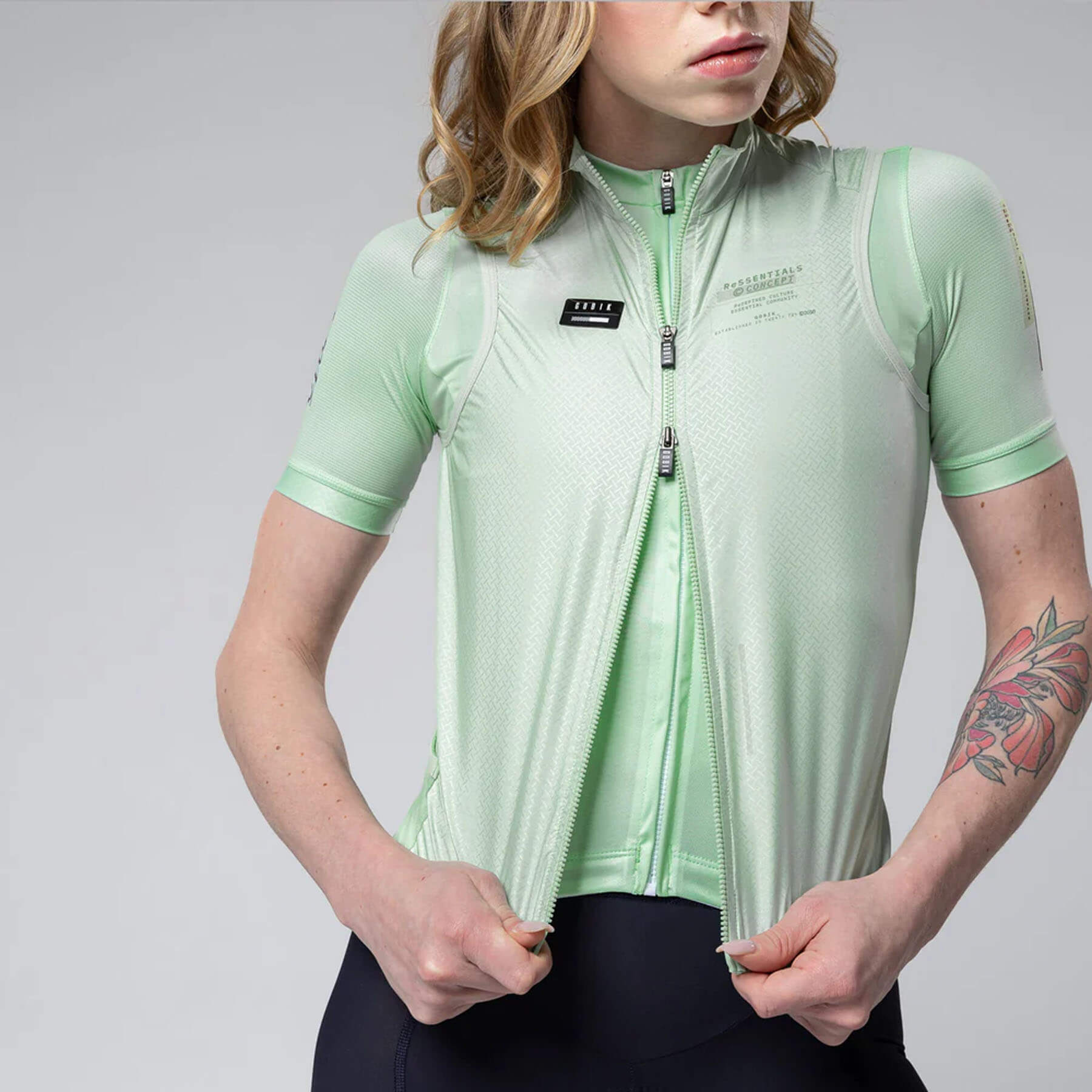 Woman wearing light green GOBIK Vest Plus 2.0 - Women's with short sleeves and front zipper on gray background