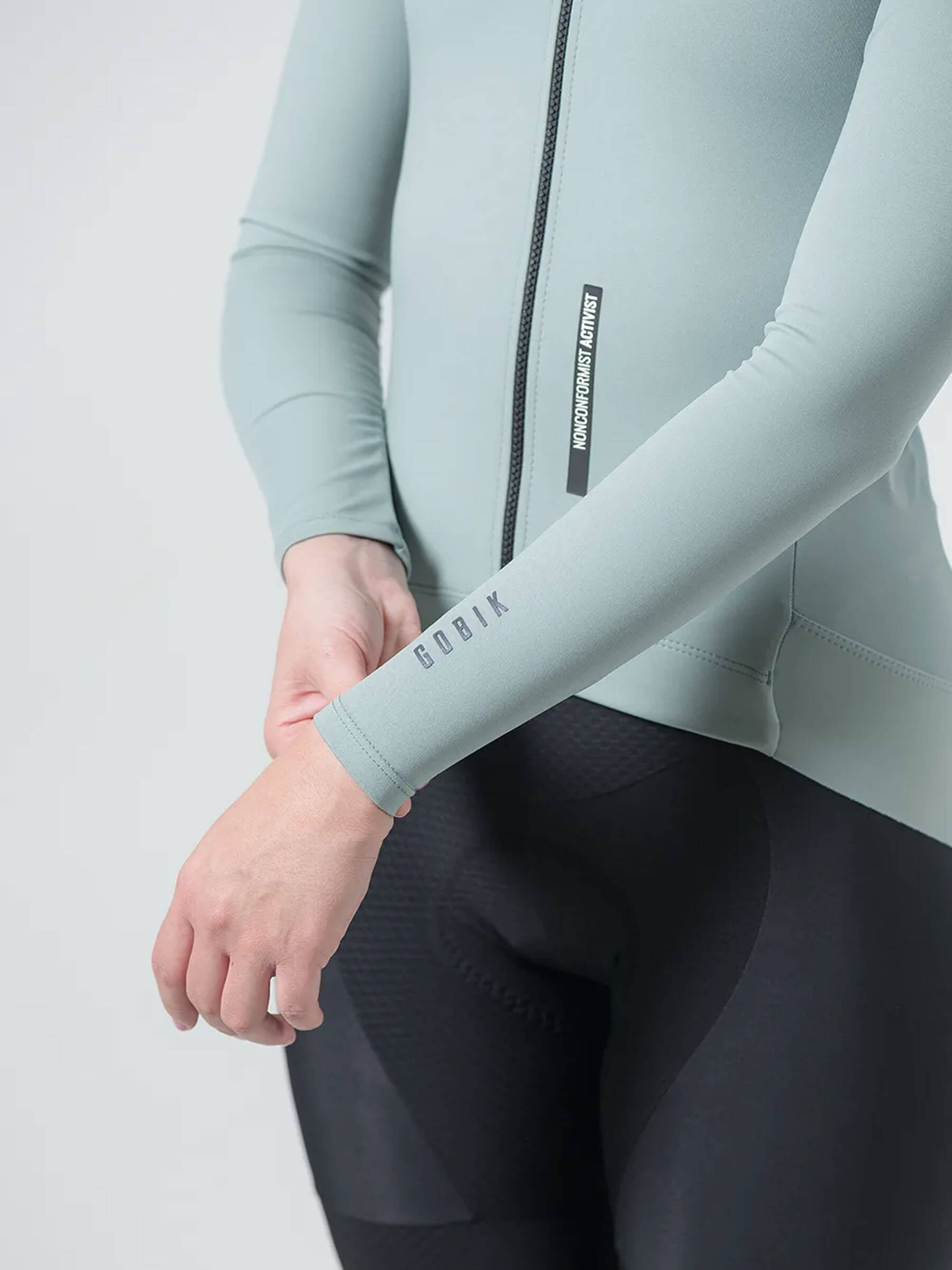 Close-up of a woman wearing GOBIK Envy Jacket - Women's in light green with logo on sleeve and front zipper details