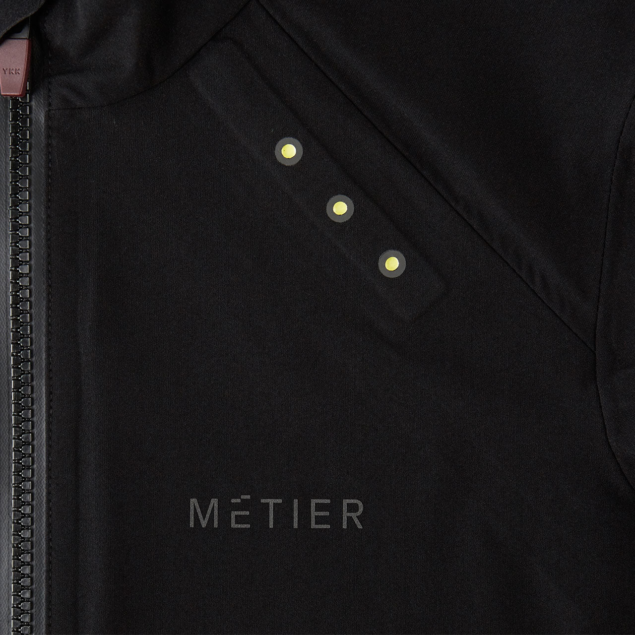 Close-up of Metier Beacon Jacket showing black fabric, front zipper, and integrated LED lights on chest area