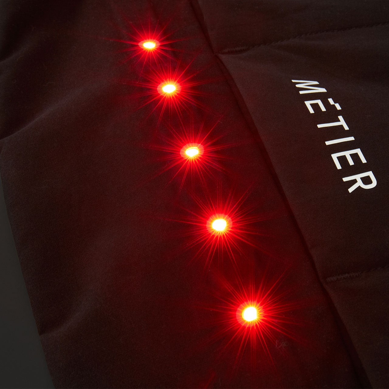 Close-up of Metier Beacon Jacket sleeve showing integrated red LED lights for enhanced cycling visibility and safety.