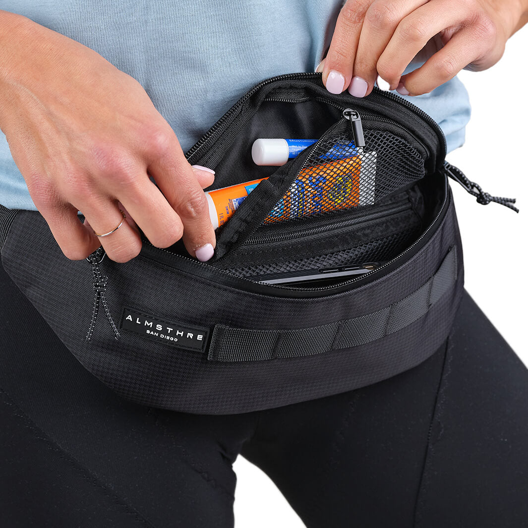 Close-up of hands opening ALMSTHRE Fanny Pack showing organized interior with mesh pocket and essentials inside