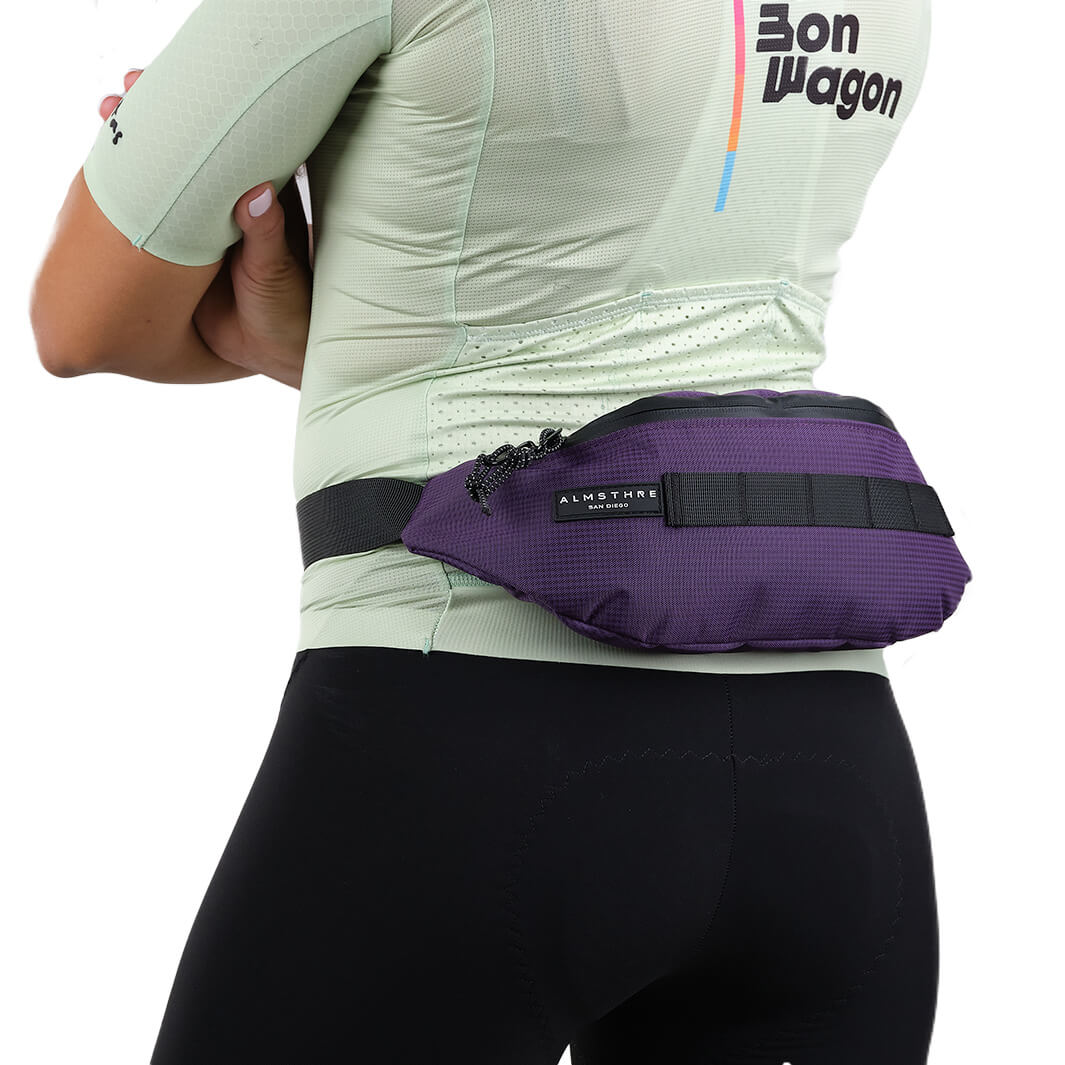 Person wearing ALMSTHRE Fanny Pack in purple with adjustable strap and sleek design shown from the back