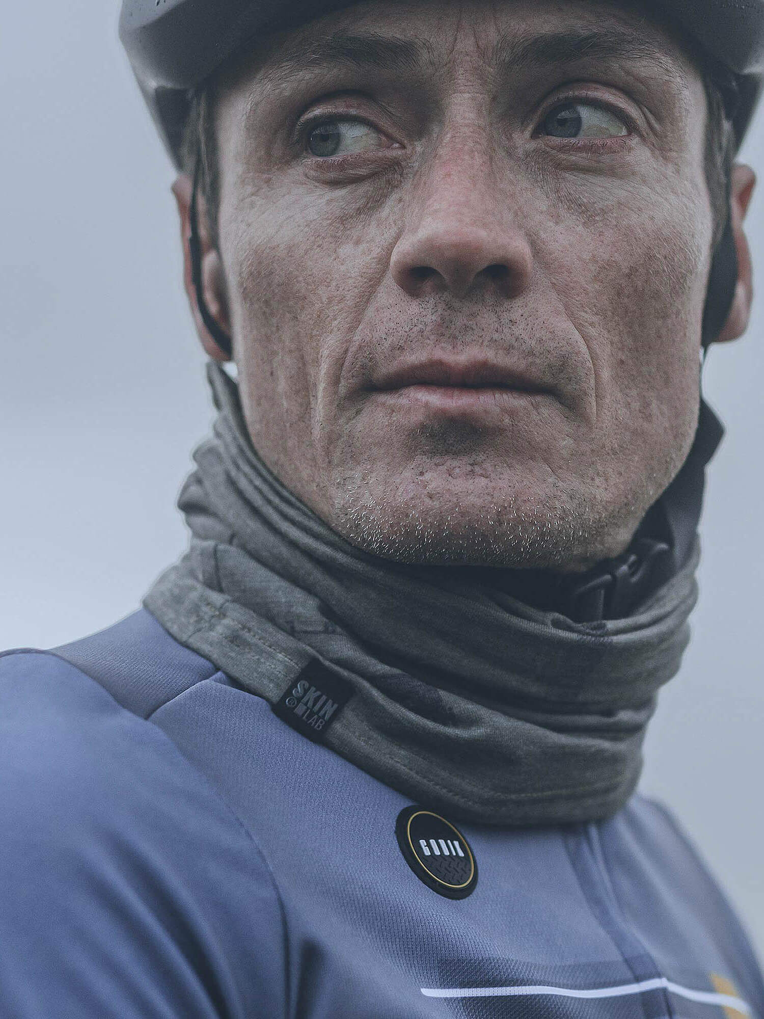Close-up of a man wearing a gray GOBIK Moonbah Merino Neck Warmer with a cycling helmet and jacket